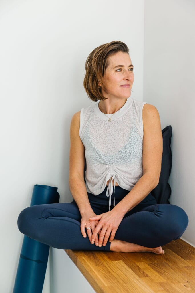 Copyright Chiara Hammerer. Portrait of Chiara Hammerer, event speaker, sitting cross-legged on a woo.